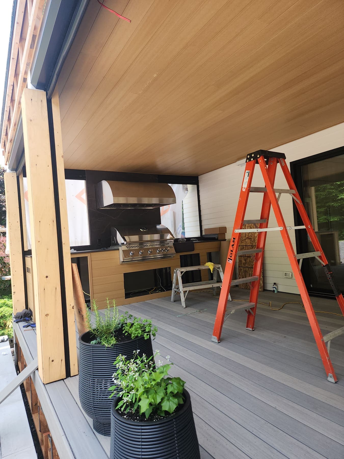 Terrasse couverte en fin de chantier : plafond en lattes de composite, cuisine extérieure avec barbecue encastré et hotte, plancher composite.